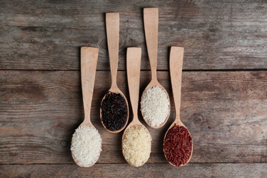 Photo of Flat lay composition with brown and other types of rice in spoons on wooden background