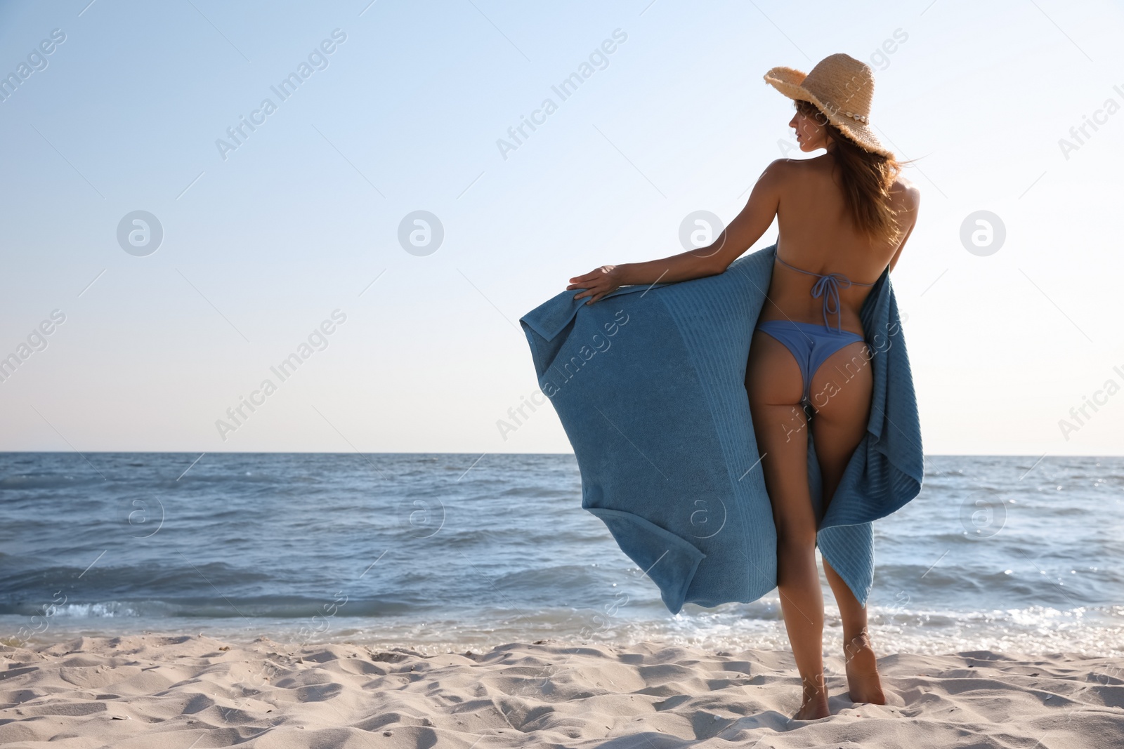 Photo of Attractive woman with beach towel and straw hat on sand near sea, back view. Space for text