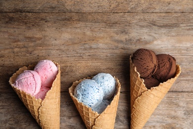 Flat lay composition with delicious ice creams in waffle cones on wooden table, space for text