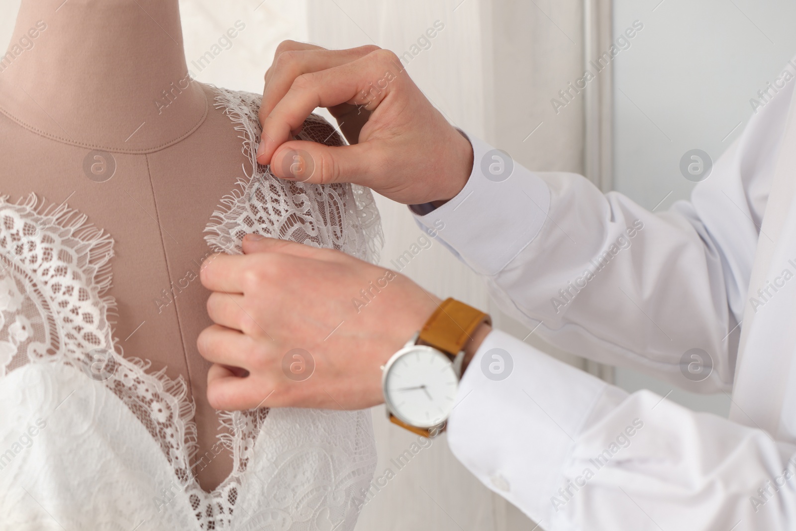 Photo of Dressmaker working with wedding dress on mannequin in atelier, closeup