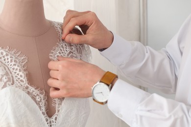 Photo of Dressmaker working with wedding dress on mannequin in atelier, closeup