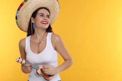 Young woman in Mexican sombrero hat playing ukulele on yellow background. Space for text