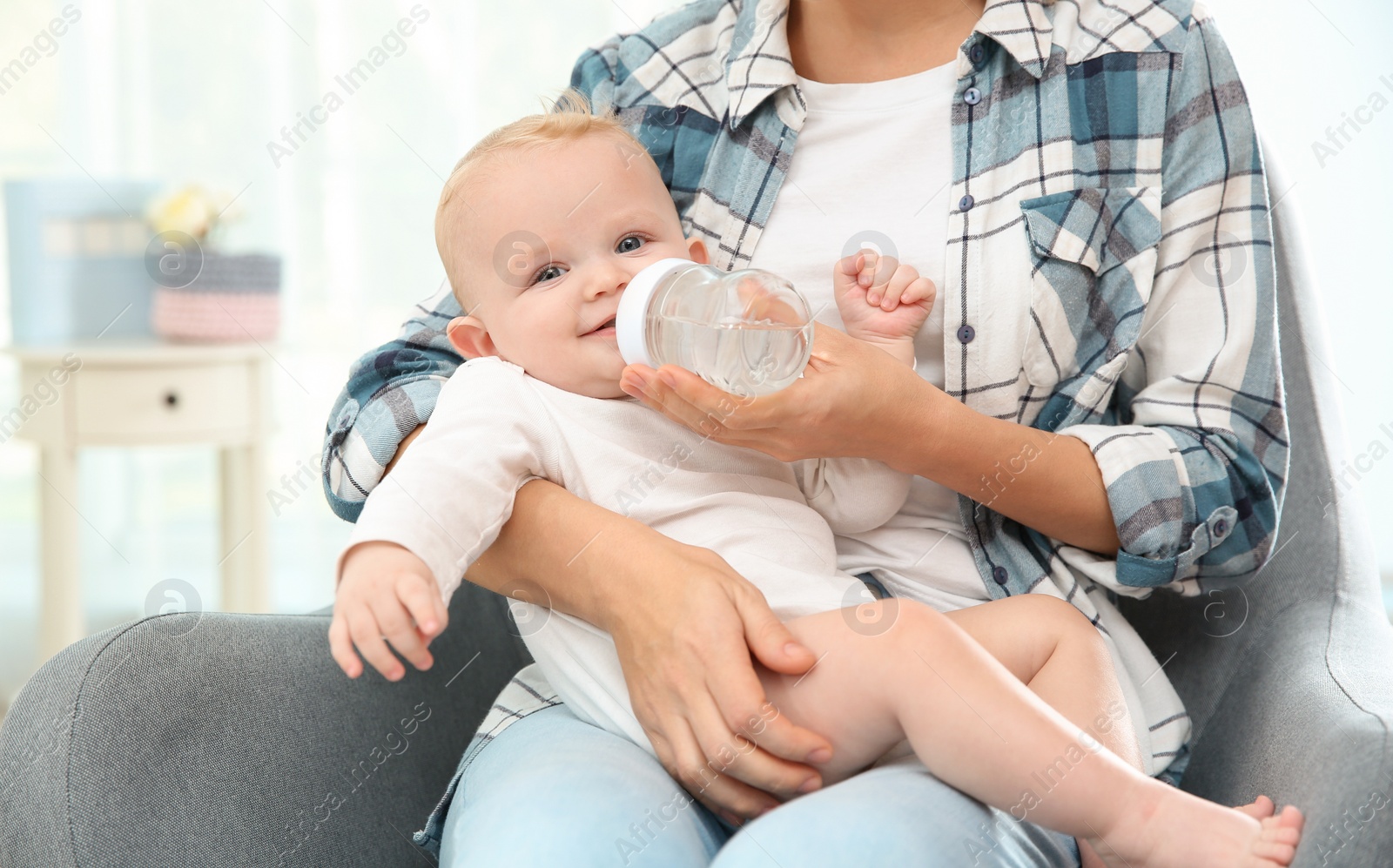 Photo of Lovely mother giving her baby drink from bottle in room