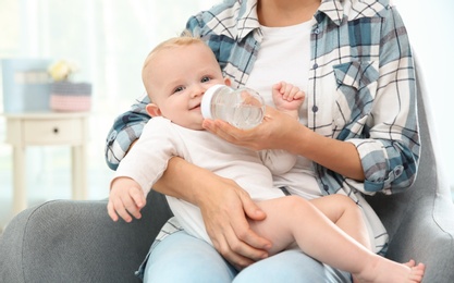 Photo of Lovely mother giving her baby drink from bottle in room