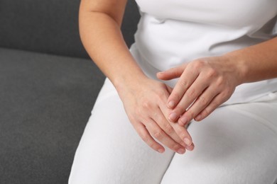 Woman applying cosmetic cream onto hand on sofa, closeup. Space for text