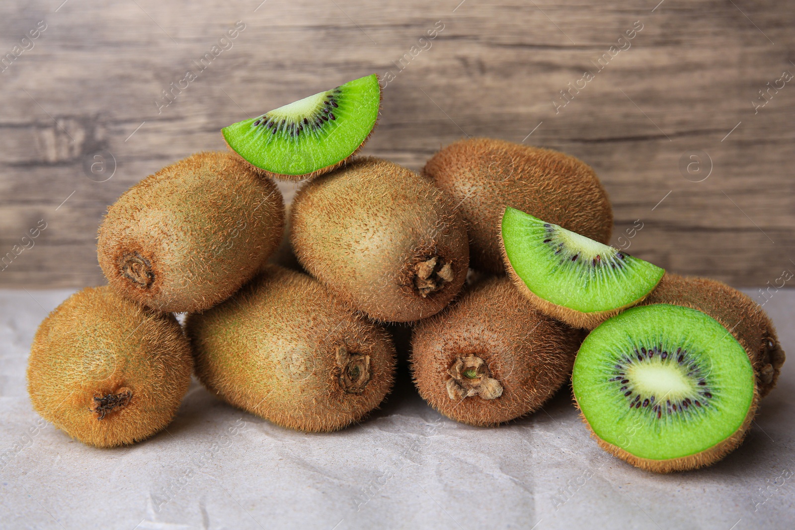 Photo of Heap of whole and cut fresh kiwis on parchment paper near wooden wall