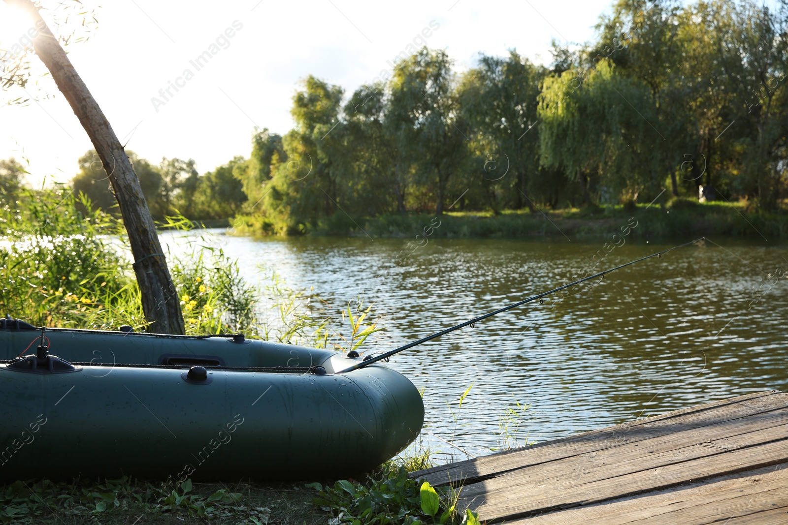 Photo of Inflatable boat with rod for fishing near wooden pier at riverside