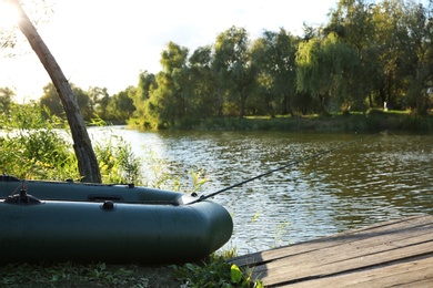 Inflatable boat with rod for fishing near wooden pier at riverside