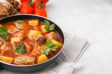Photo of Delicious goulash in saucepan on white tiled table, closeup. Space for text