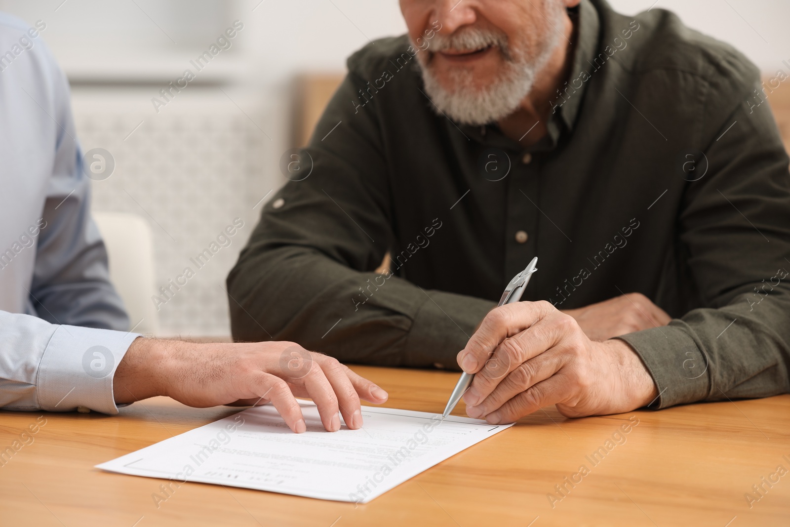 Photo of Notary showing senior man where to sign Last Will and Testament at wooden table indoors, closeup