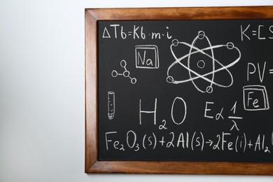 Photo of Blackboard with different chemical formulas written with chalk on white wall. Space for text