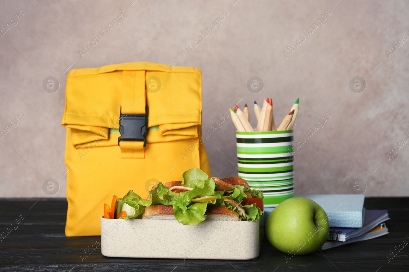 Photo of Healthy food for school child and stationery on table near color wall