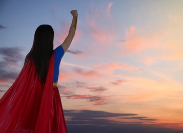 Image of Confident woman wearing superhero costume against cloudy sky, back view. Space for text