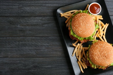 Plate with tasty burgers, french fries and sauce on wooden background, top view. Space for text