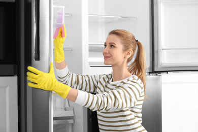 Woman in rubber gloves cleaning empty refrigerator at home