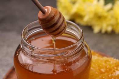 Photo of Pouring sweet golden honey from dipper into jar at table, closeup