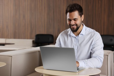 Happy young man working on laptop at table in office. Space for text