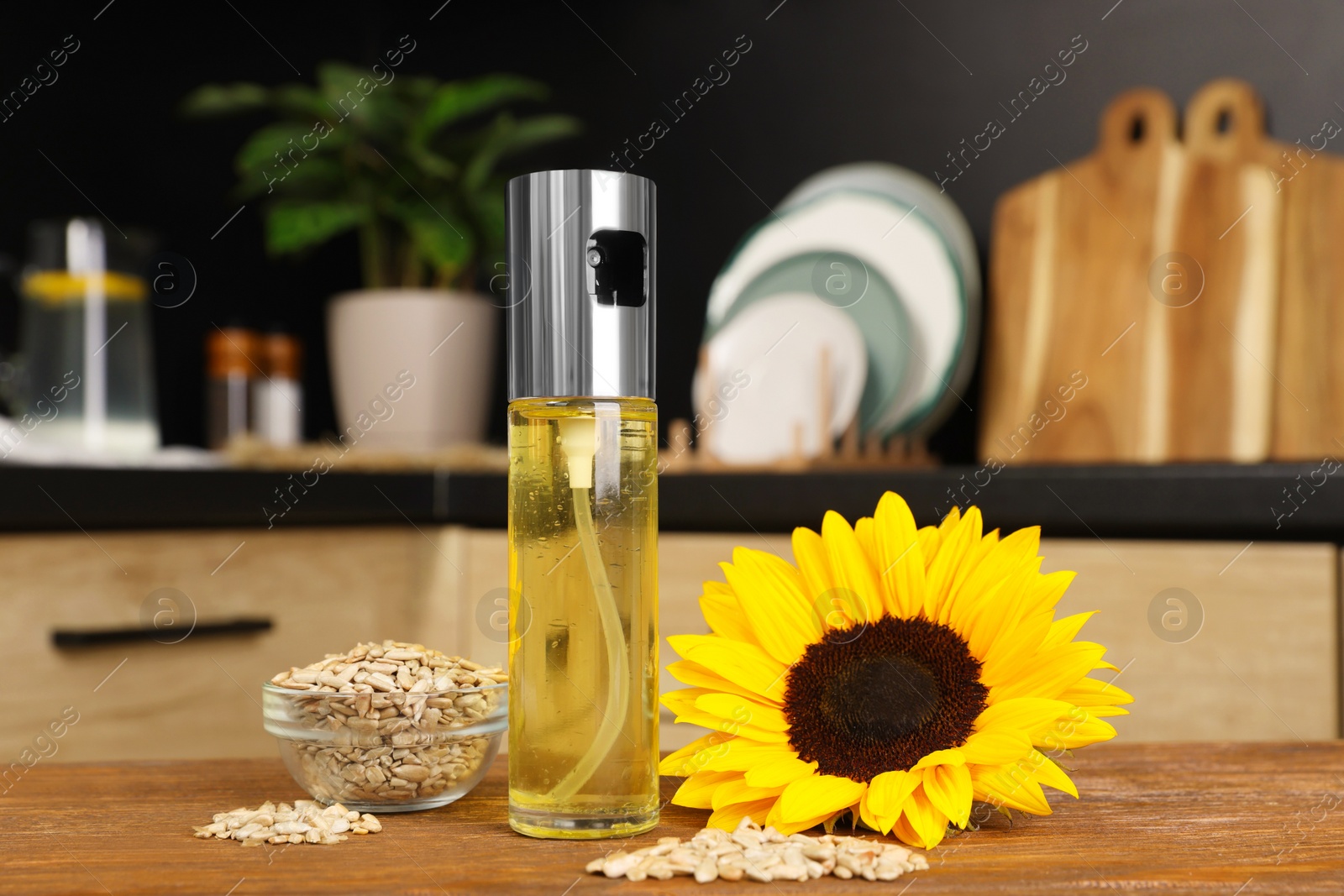 Photo of Sunflower, seeds and spray bottle with cooking oil on wooden table in kitchen