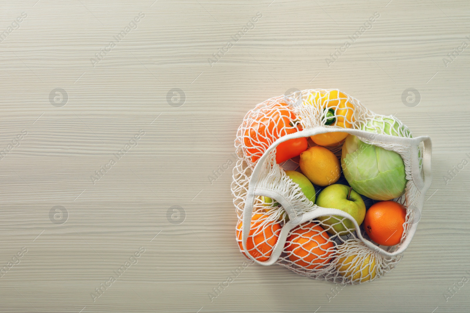 Photo of Net bag with vegetables and fruits on wooden table, top view. Space for text