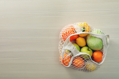 Photo of Net bag with vegetables and fruits on wooden table, top view. Space for text