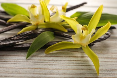 Photo of Vanilla pods, beautiful flowers and green leaves on white wooden table, closeup