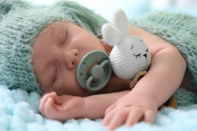 Cute newborn baby with pacifier sleeping on light blue blanket, closeup