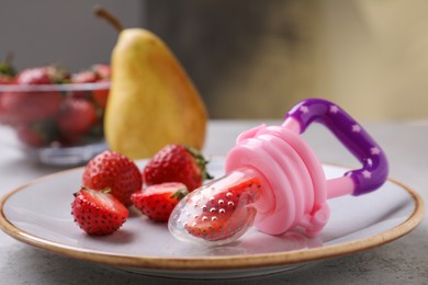 Photo of Plastic nibbler with fresh strawberries on light table, closeup. Baby feeder