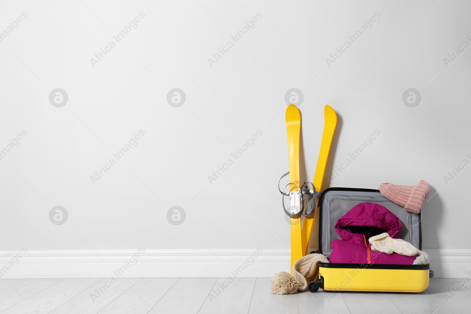 Photo of Open suitcase with warm clothes for winter vacation on wooden floor. Space for text