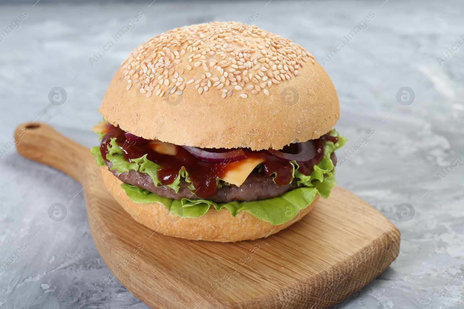 Photo of Delicious cheeseburger with lettuce, onion, ketchup and patty on grey table, closeup