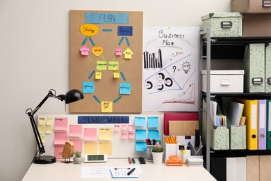 Photo of Business process planning and optimization. Workplace with lamp, colorful paper notes and other stationery on white wooden table