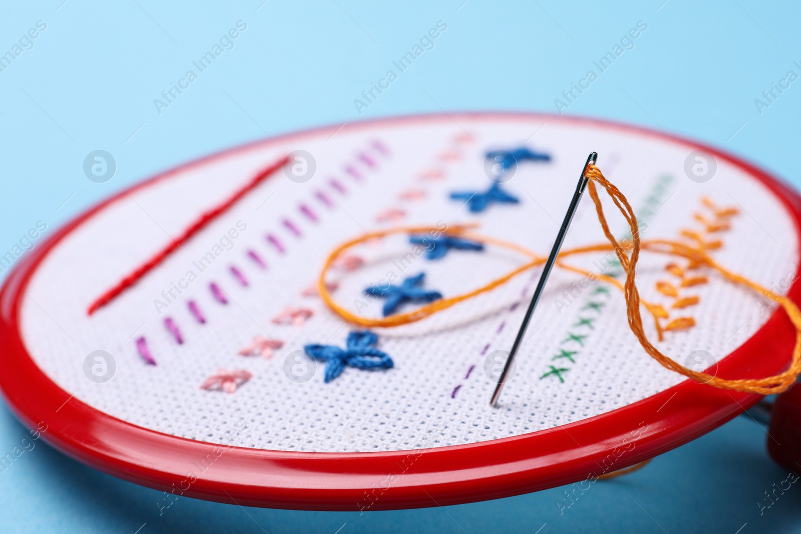 Photo of Embroidery hoop with fabric and needle on light blue background, closeup