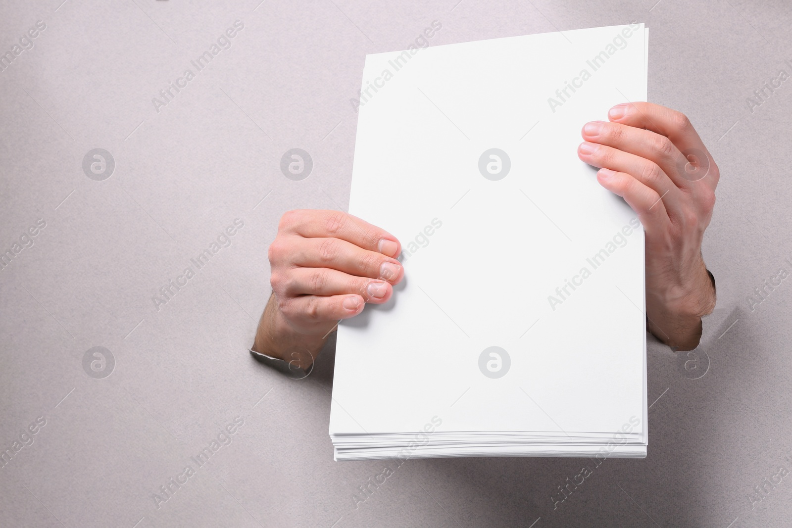 Photo of Man holding sheets of paper through holes in white paper, closeup. Mockup for design