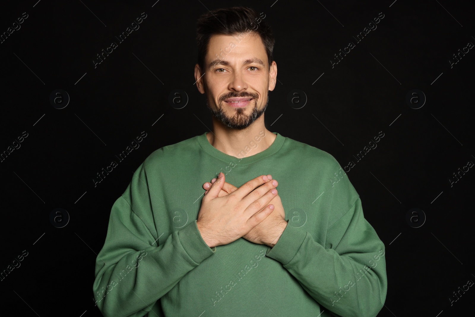 Photo of Man with clasped hands praying on black background