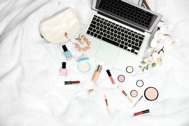Flat lay composition with laptop and makeup products for woman on bed