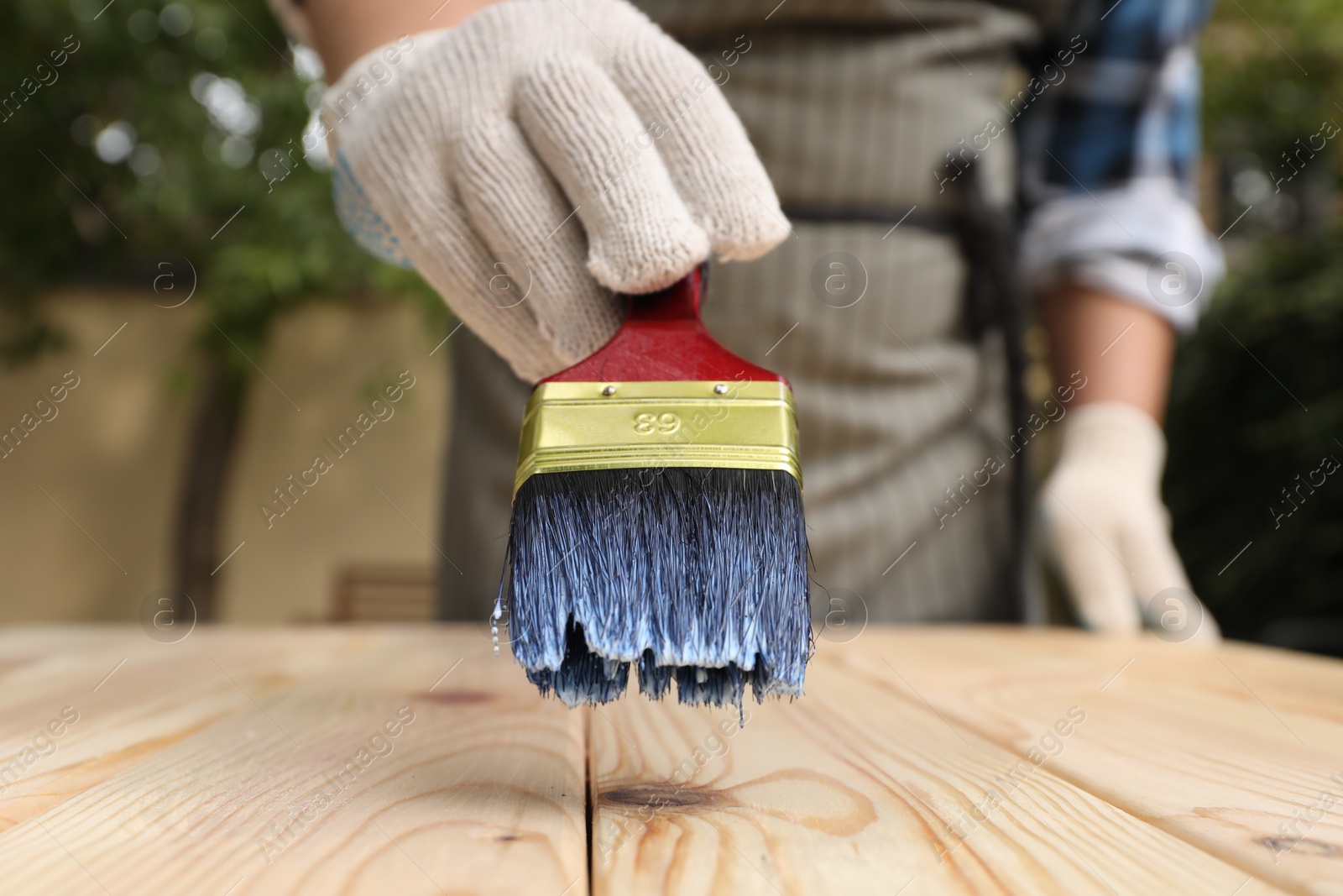 Photo of Man varnishing wooden surface with brush outdoors, closeup