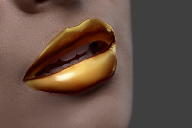 Image of Young woman with beautiful gold lips on grey background, closeup