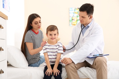 Children's doctor examining little patient with stethoscope at home