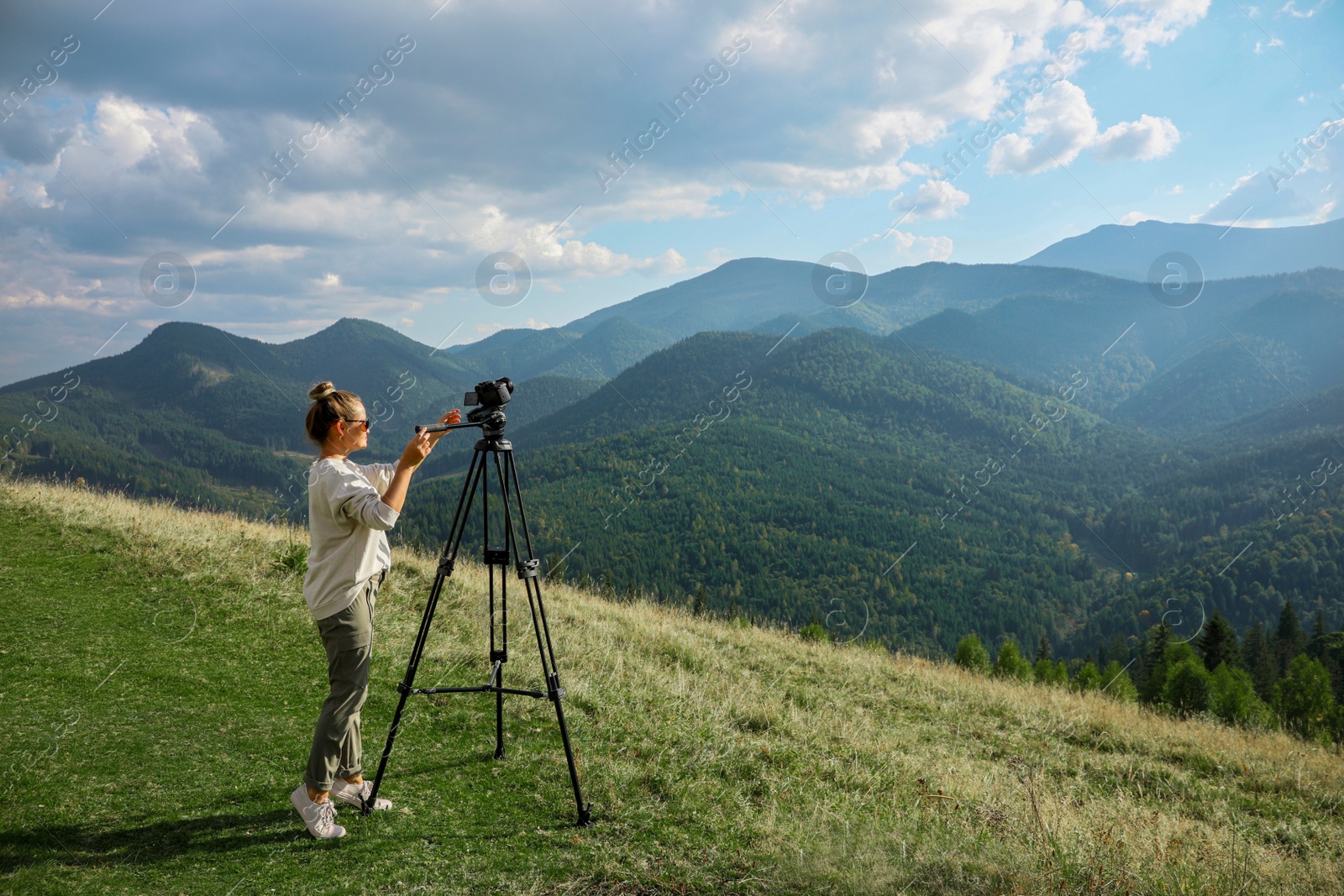 Photo of Professional photographer with modern camera on tripod in mountains. Space for text