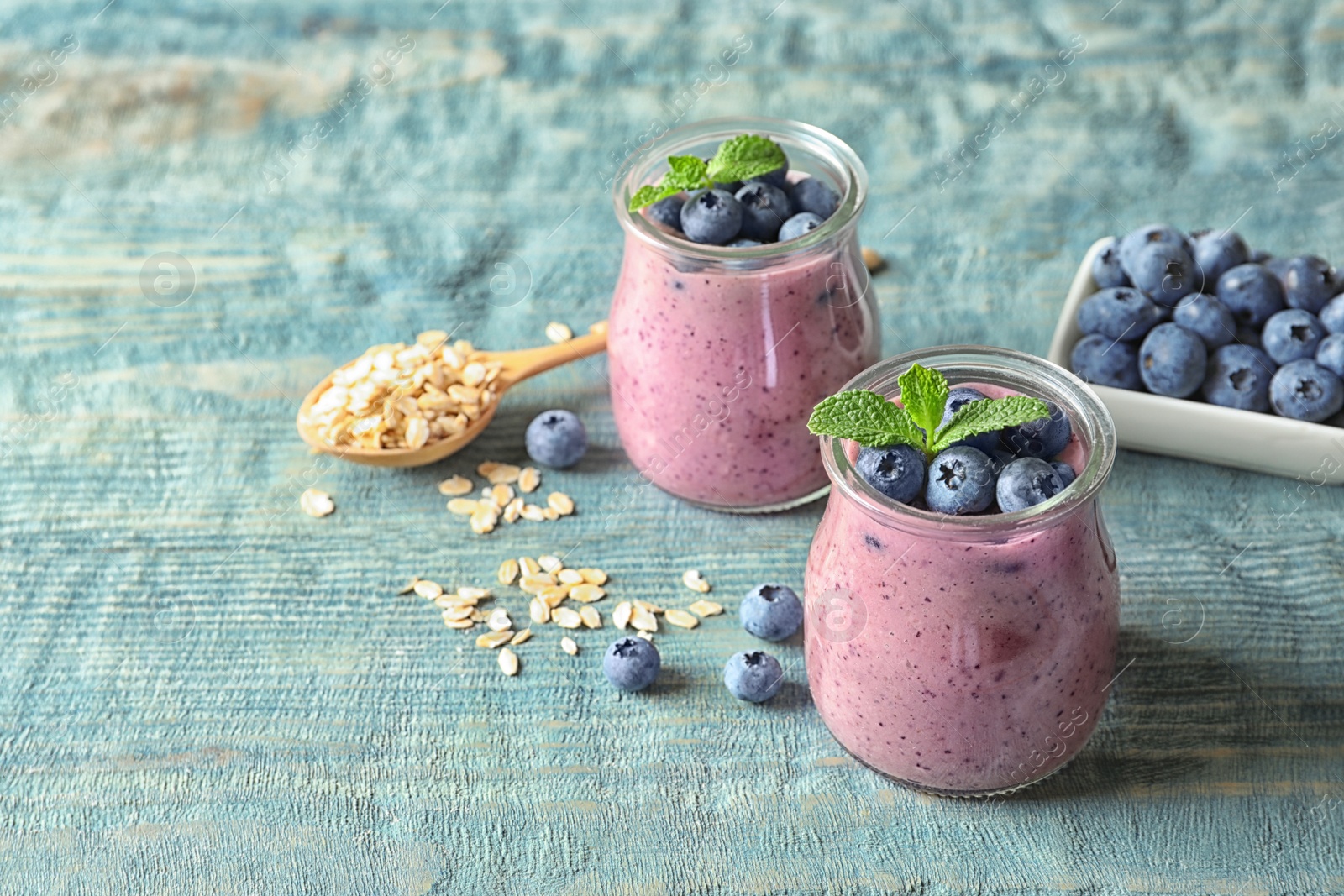 Photo of Tasty blueberry smoothie in jars, berries, oatmeal and space for text on wooden table