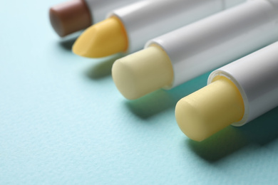 Different hygienic lipsticks on turquoise background, closeup