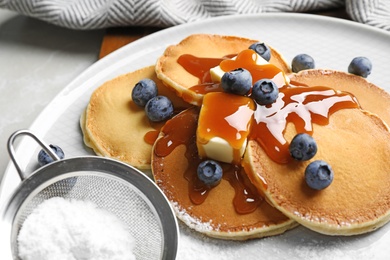 Delicious pancakes with fresh blueberries, butter and syrup on light grey table, closeup