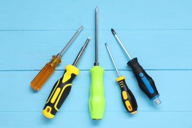 Group of different screwdrivers on light blue wooden table, top view