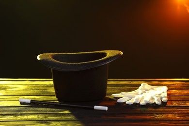 Photo of Magician's hat, wand and gloves on wooden table against dark background