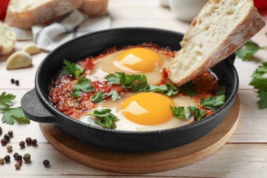 Photo of Delicious shakshuka with bread in frying pan on light wooden table, closeup