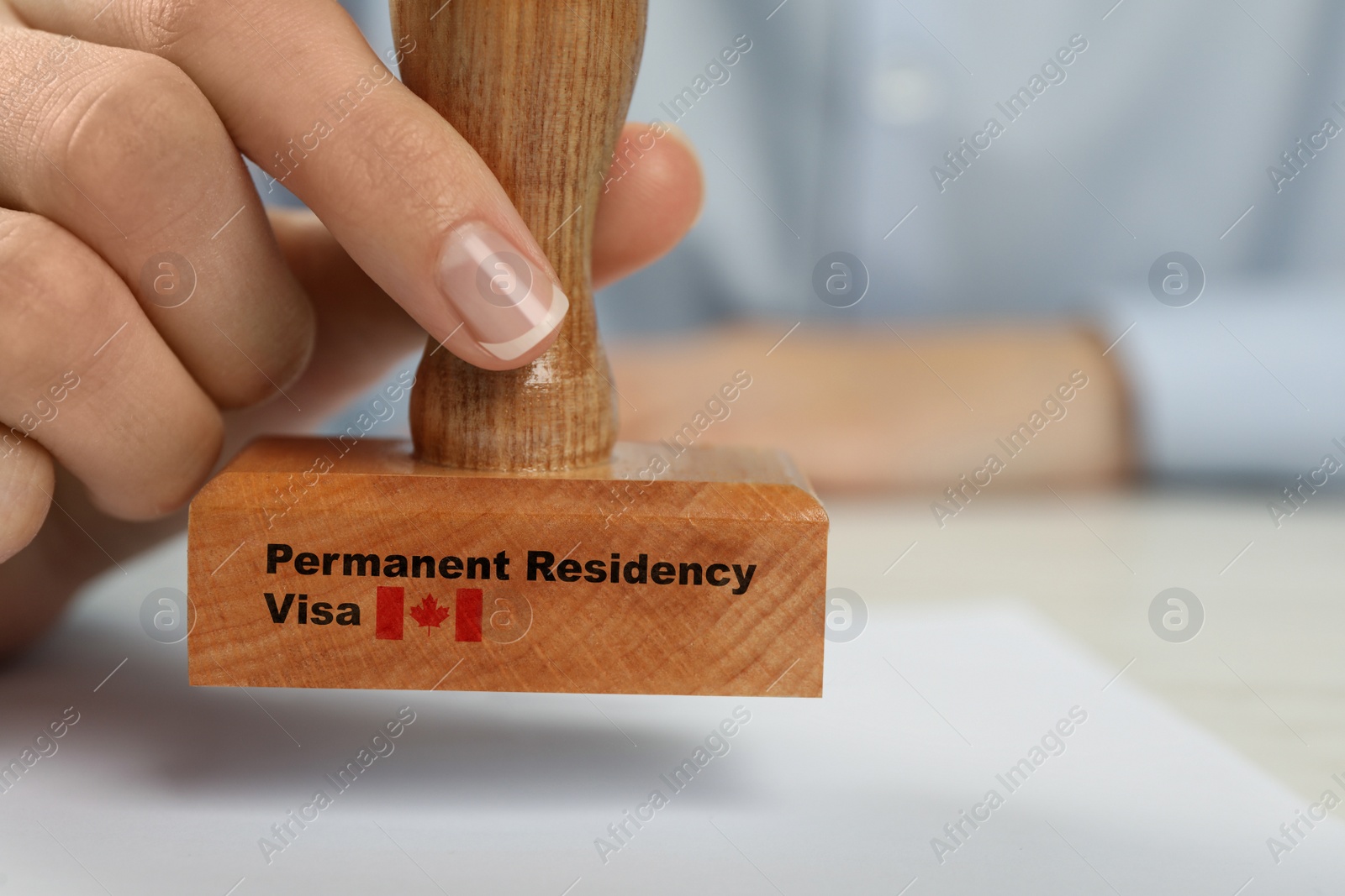 Image of Woman stamping document at white wooden table, closeup. Permanent residency visa in Canada