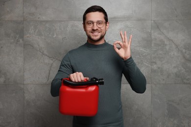 Man holding red canister and showing OK gesture near grey wall
