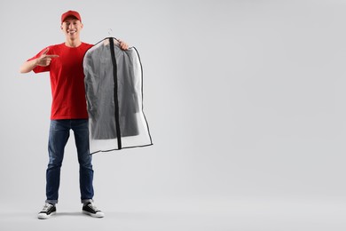 Dry-cleaning delivery. Happy courier holding garment cover with clothes on light grey background, space for text