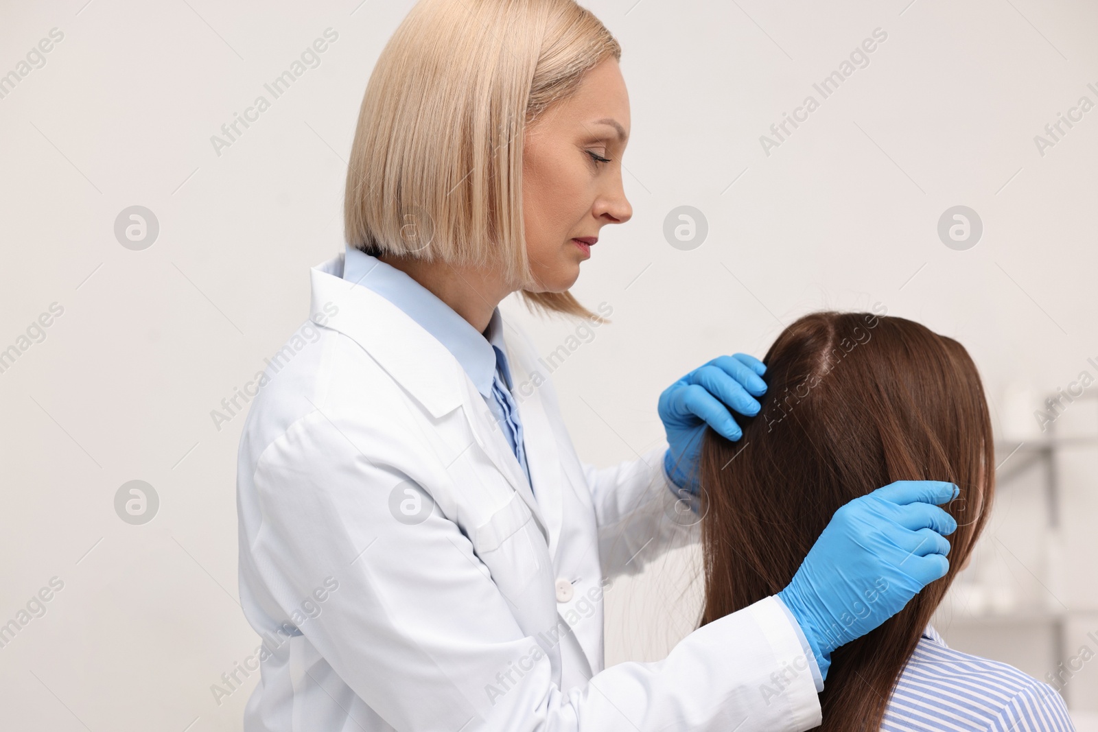 Photo of Trichologist in gloves examining patient`s hair in clinic