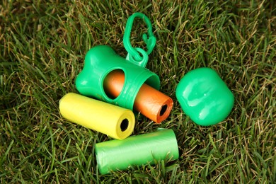 Photo of Rolls of colorful dog waste bags on green grass outdoors, above view
