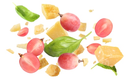 Pieces of delicious parmesan, grapes and basil leaves falling on white background